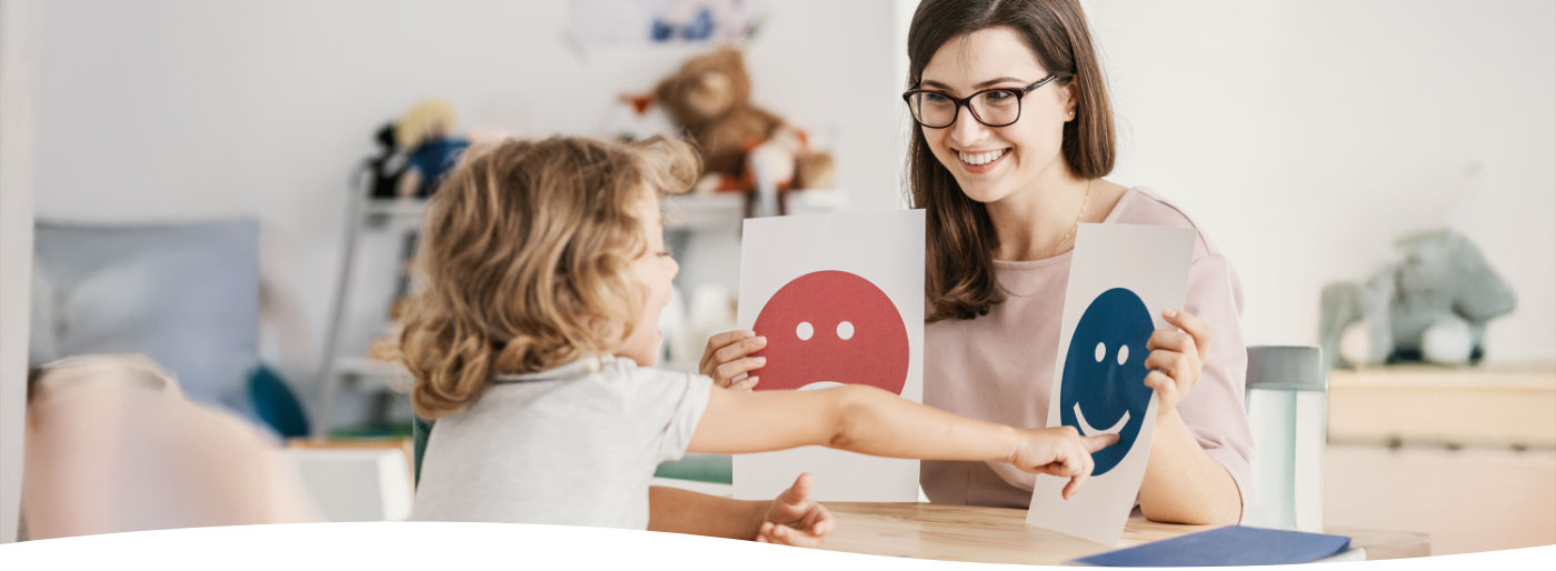 Eine Assisten:in zeigt einem Kind Emoticons zur Auswahl